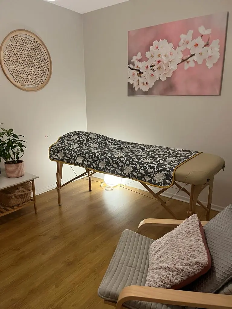 image de la salle de soin pour les pratiques des soins avec chaise de relaxation et table de massage , ambiance détente avec un tableau de cerisier et un tableau la fleur de vie